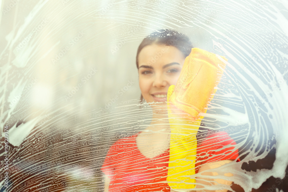 Young woman washing window glass with duster inside