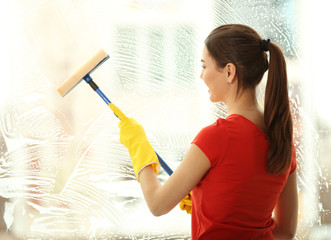 Canvas Print - Young woman washing window glass with sponge mop indoors