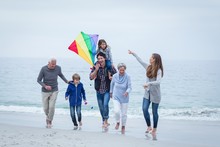 Multi-generation Family Running At Sea Shore Against Sky
