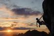 Silhouette of beautiful athletic woman climbing steep rock wall against amazing sunset scene in the mountains. Girl is hanging on one hand and looking up.