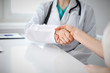 © rogerphoto - Handshake doctor and patient sitting at the table, closeup