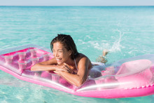 Beach Girl Having Fun Splashing Water In Ocean Floating On Pink Pool Float Toy Air Mattress. Asian Woman Relaxing In The Sun Swimming In The Perfect Turquoise Sea At Holiday Resort.