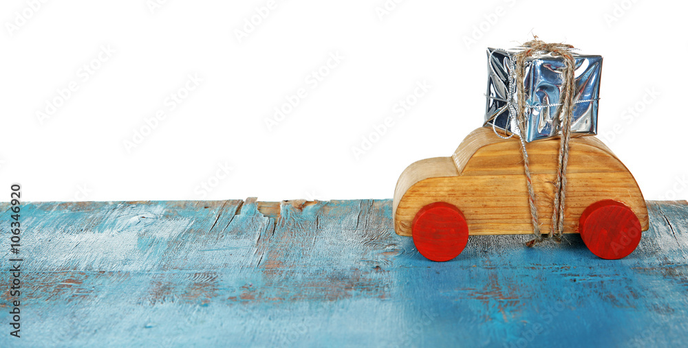 Wooden toy car with gift box on a table over white background