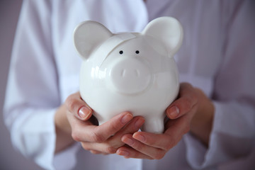 Canvas Print - Woman holding in hands white piggy bank with patch