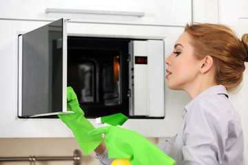 Wall Mural - Young woman cleaning microwave with a sponge