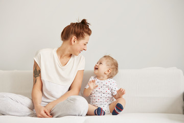 young mother with her one years old little son dressed in pajamas are relaxing and playing in the be