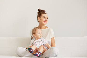 young mother with her one years old little son dressed in pajamas are relaxing and playing in the be