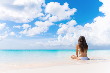 Wall Mural - Beach vacation dream woman enjoying summer holiday on dreamy perfect ocean tropical destination. Person sitting from the back alone on deserted white sand beach getaway.