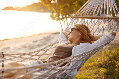 Fotografía Hermosa niña en una hamaca en la playa, mirando la puesta de sol
