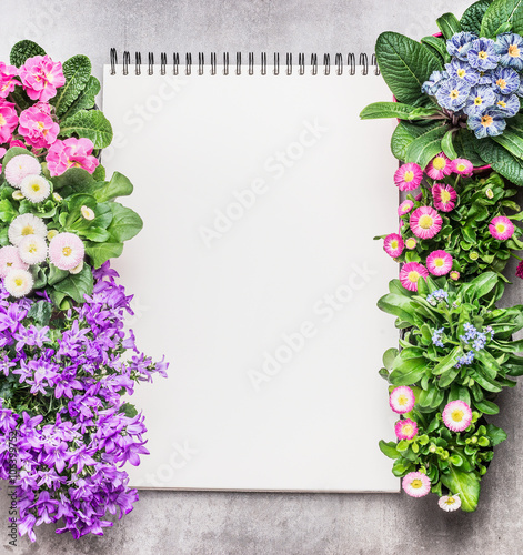 Notebook with garden flowers in pots on stone background