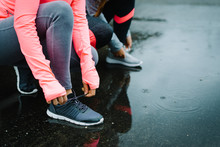 Urban Athletes Lacing Sport Footwear For Running Over Asphalt Under The Rain. Two Women Getting Ready For Outdoor Training And Fitness Exercising On Cold Winter Weather.