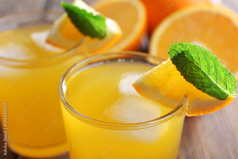 Two orange juices with ice and orange on, closeup