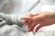 © Africa Studio - Little baby boy in grey pajamas holding mother's hand on the bed, close up