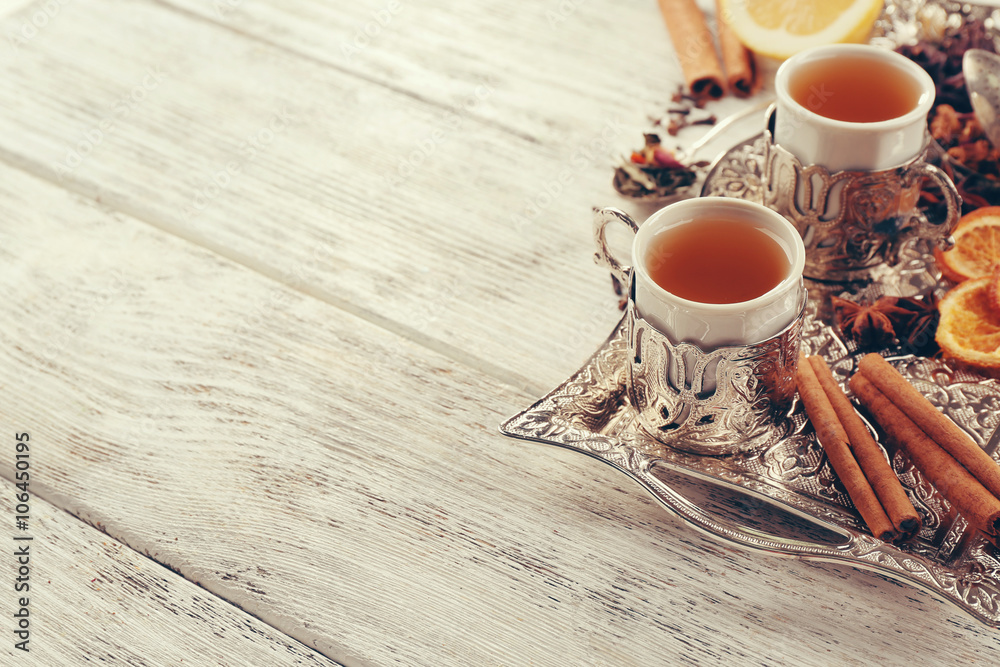 Two cups of brewed tea with spices on light wooden table