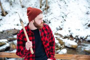 Wall Mural - Pensive man in checkered shirt holding axe at winter forest