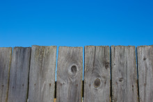 Old Wooden Fence And A Blue Sky. Wooden Planks On A Background Of Pure Clear Sky. Front View. Copy Space For Your Text