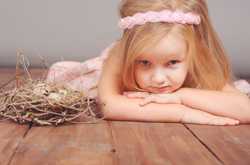 cute little girl lying on the floor with bird nest. looking at camera.