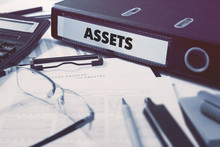 Assets - Office Folder On Background Of Working Table With Stationery, Glasses, Reports. Business Concept On Blurred Background. Toned Image.