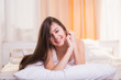 © F8  \ Suport Ukraine - Vivacious young woman in bed lying on the bedclothes on her stomach with her chin on her hands giving the camera a beautiful smile