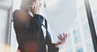 © SFIO CRACHO - Business woman wearing white shirt, talking smartphone and holding documents in hands. Loft office. Panoramic windows background. Wide mockup, film effect, bokeh