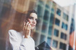 © SFIO CRACHO - Photo business woman wearing modern white shirt, talking smartphone and holding documents in hands. Open space loft office. Panoramic windows background. Horizontal mockup. Film effect