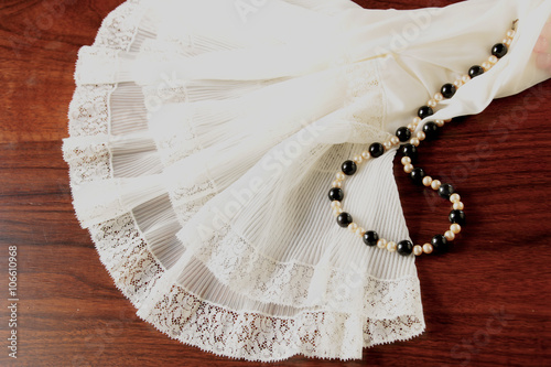 Fotografie, Obraz A lace petticoat and a black and white pearl necklace on a brown, wooden table