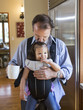 © Sam Diephuis/Blend Images - Father holding daughter in sling in kitchen