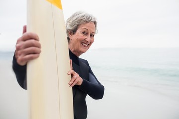 Wall Mural - Senior woman in wetsuit holding a surfboard on the beach