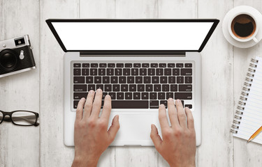Poster - Man work on laptop with isolated white screen for mockup. Work desk with camera, glasses, coffee, notepad and pencil beside on wooden table. Top view.