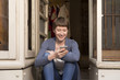 © Westend61 - Portrait of female fashion designer with smartphone sitting at the entrance of her studio