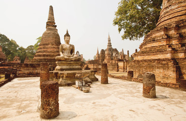 Brick pagoda and ancient ruined columns of temple Wat Maha That with Buddha statue