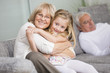 © Westend61 - Portrait of senior woman hugging granddaughter on sofa in living room
