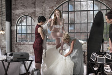 Mother And Bridesmaid Helping Bride Putting On Wedding Dress