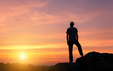 Wall Mural - landscape with silhouette of a standing man on the background of colorful yellow sky on the rock at 