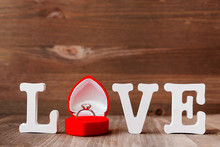 Word LOVE And Diamond Engagement Ring In Red Gift Box On Wooden Background.