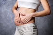 © Africa Studio - Pregnant woman making heart with her hands on grey wall background
