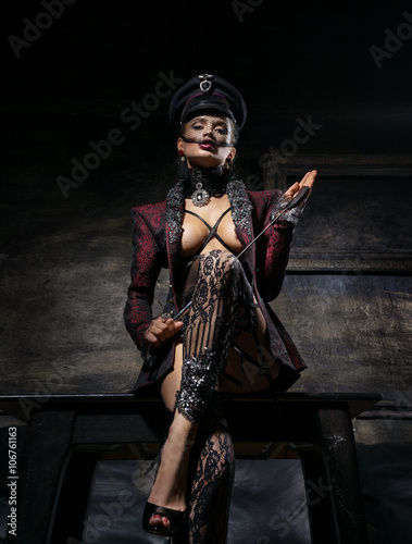 Fotografia Girl in a beautiful cap and a jacket standing near the wall with a whip