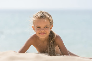six-year tanned girl lying on sand, leaning on hands against the sea