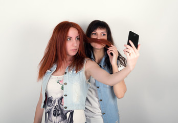 beauty hipster girls with a headphones, make selfie on a phone. teenagers grimace. Two young girlfriends indulge and grimace, make each other a mustache out of the hair