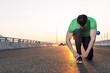 Urban jogger tying his running shoes on a big bridge. sunset hig
