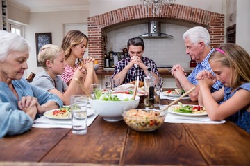 Multi-generation family praying before having meal