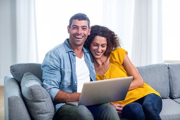 Wall Mural - Young couple sitting on sofa and using laptop