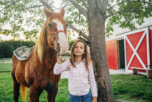 Caucasian Girl Walking Horse Outside Barn On Farm