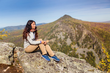 Wall Mural - Young woman hiker sitting on cliff's edge and looking to a blue