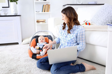 Wall Mural - Beautiful woman with baby boy working from home using laptop