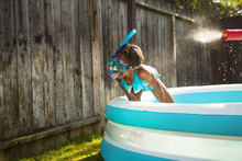 Girl In Scuba Mask Getting Sprayed With Water Gun In Garden Paddling Pool