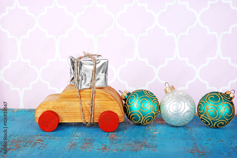 Wooden toy car with gift box and baubles on a table over pattern background