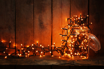 Wall Mural - Glass jar with lighted garland on wooden background