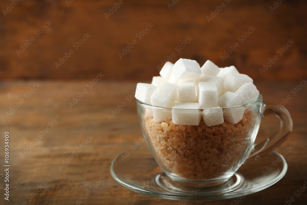 Glass cup with lump and brown sugar on wooden background