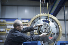 Engineer Using Crane To Move Large Gear Wheel In Engineering Factory